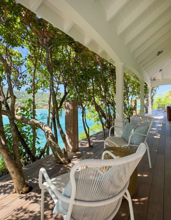villaervr_xanadu-30 Wooden balcony with white lounge chairs shaded by trees overlooking a tropical bay.